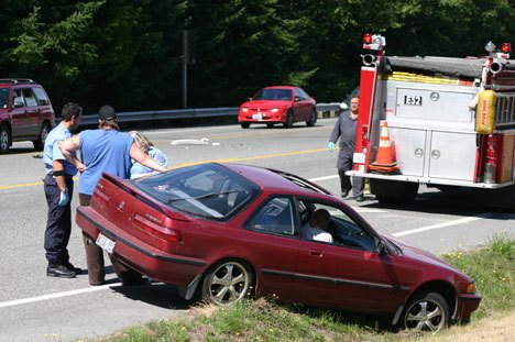 EMTs talk to a man next to a vehicle involved in a two-car crash on Highway 525 at Ken's Korner Wednesday.