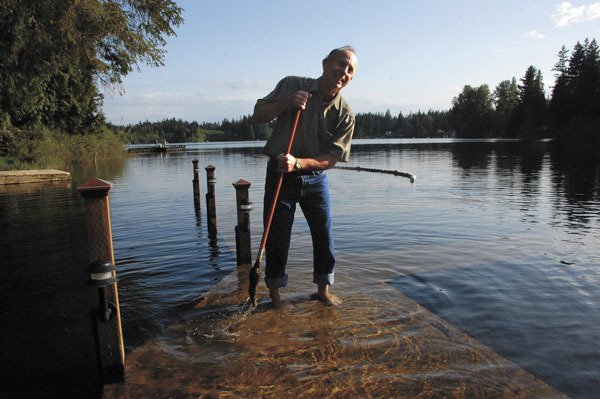 Deer Lake resident Curt Gordon sweeps slime from a submerged dock. Lake levels are high for this time of year and residents worry that the opening of water skiing season