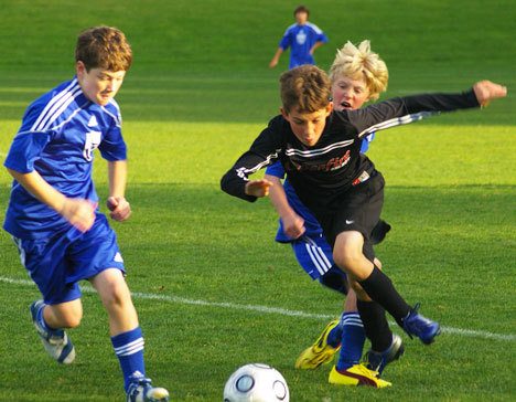 U-13 Revolution soccer players Parker Buchanan (left) and Quinn Hassrick (behind Crossfire player) play aggressive defense against the Crossfire forward.