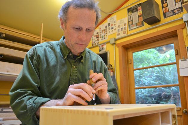 John Shinneman carves his name into a cabinet which is part of the piece he is showing at Woodpalooza.