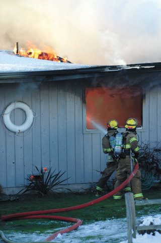 Firefighters pour water on a Sunlight Beach house that caught fire Monday morning. The fire also spread to another house next door.