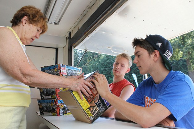 Zach Soto inspects a fireworks package with friend Bjorn Elliott at the Kiwanis of South Whidbey stand at Ken’s Korner in Clinton. Nancy Tipton