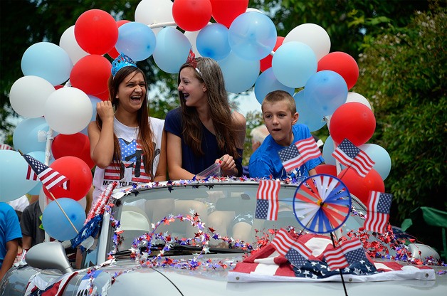 A few children laugh atop a convertible during the 2014 Maxwelton Independence Day Parade adorned in the red