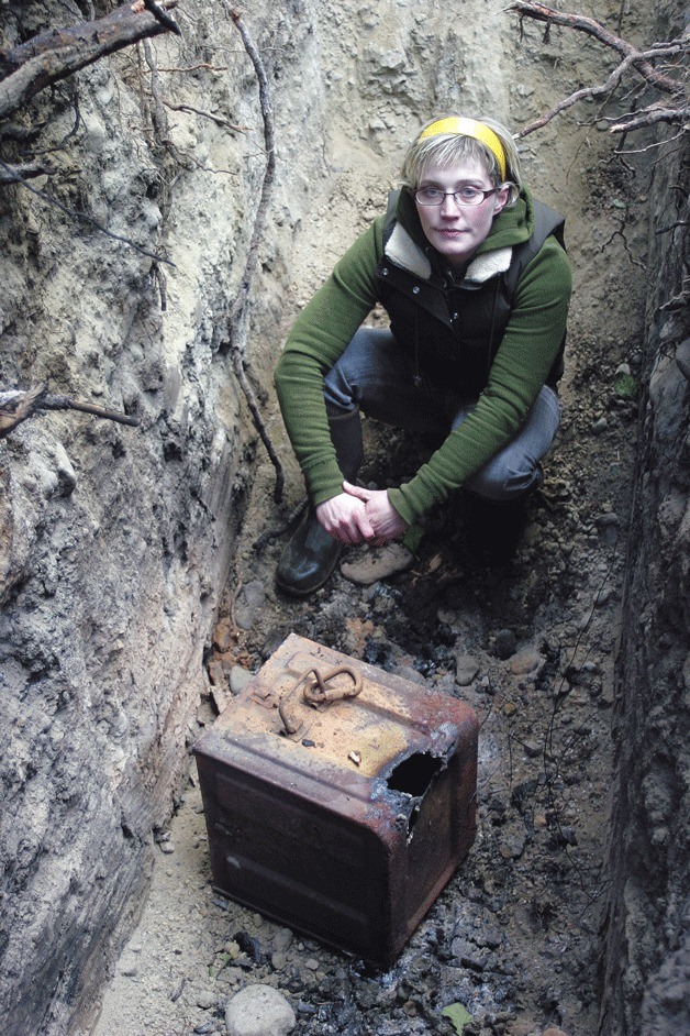 Kristen Aley sits in a trench near her parents’ Lone Lake home with the remains of a box of dynamite she found nearby. The unstable material was placed in the trench and burned Wednesday by a Navy explosives team.
