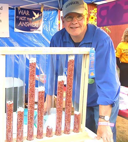 Hometown Hero Tom Ewell stand next to his “bean poll” at the Whidbey fair. The dedicated peacemaker uses it as a tool to demonstrate federal budget priorities and the great amount that goes toward defense spending.