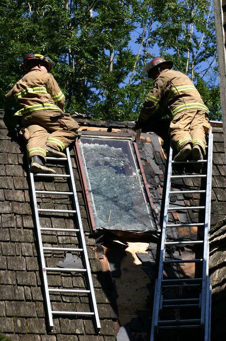 Fire District 3 firefighters Brandon Callahan and Forrest Hughes clear scorched material away from a skylight at the scene of a house fire on Windfall Road in Clinton on Friday afternoon.