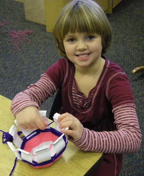 Elementary school student Ellie Thompson practices basket-weaving in a kindergarten art docent led art session.