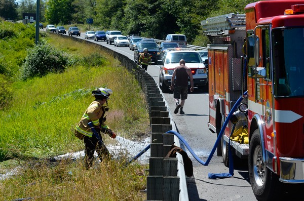 South Whidbey Fire/EMS Division Chief Wendy Moffatt hoses down a small brush fire on the side of Highway 525 in Freeland Wednesday afternoon. Low moisture levels and hot days have spurred the Island County Sheriff's Office to announce a modified burn ban