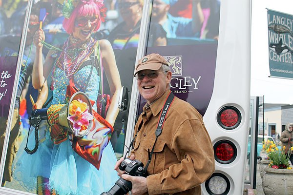South Whidbey photographer David Welton poses for a picture next to a Whidbey SeaTac Shuttle decorated with an image he shot last year.