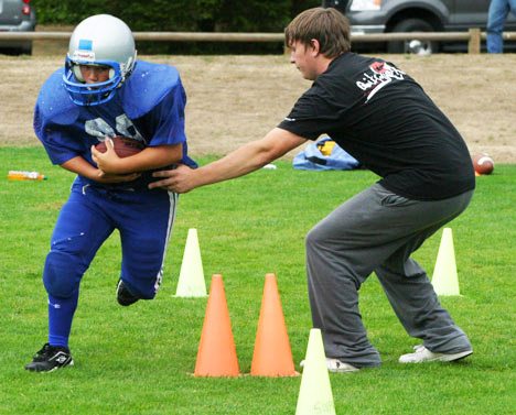 Volunteer coach Corey Soto hands off to budding tailback Hunter Kohl during a drill at Community Park Monday. The SWYF Islanders will play their first home game on Sept. 12.