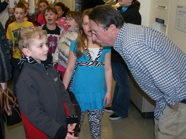Langley Postmaster Jack Harrington listens to a question posed by Ronin Fisher as other second graders mingle behind them in the post office lobby.
