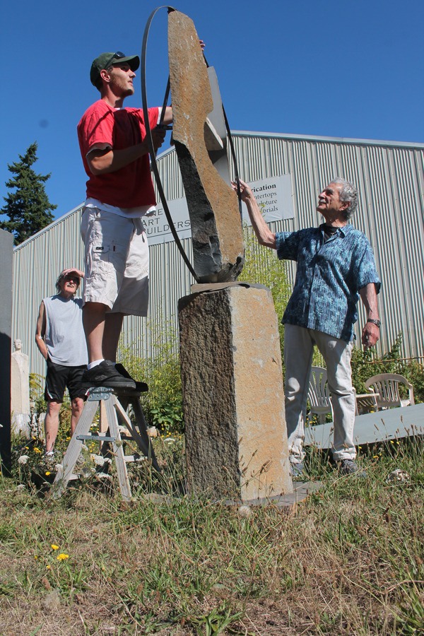 Frank Rose holds a band in place while stone fabricator Justin Haffner tries to clamp it atop a piece in progress by Lloyd Whannell. Behind them is Hank Nelson