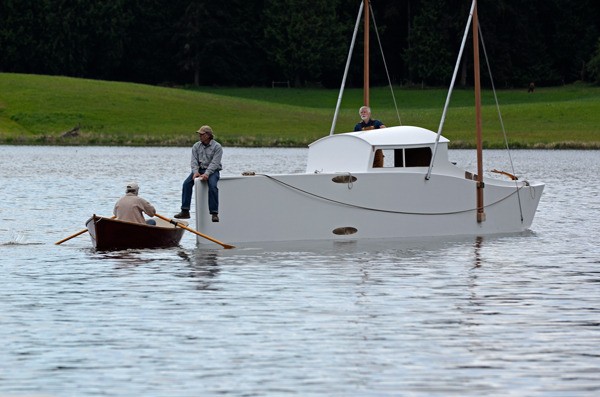 Freeland wooden boat builder Brad Rice sits on the bow of a 52-foot folding boat he built for Bob Kertell (right) during a soft launch on Lone Lake last week.