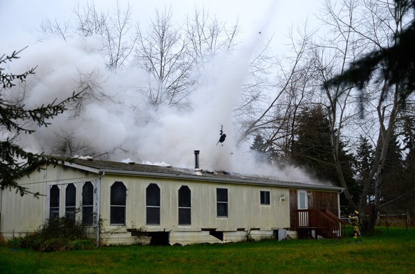 A South Whidbey Fire/EMS firefighter (below right) stands ready with a firehose as fellow firefighters (out of sight) shoot flames in the roof. The force was water was so great it shot through the roof itself.