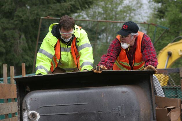 Louis Foote and Tim Economu maneuver a bathtub off a truck at the debris collection yard in Clinton for the Hearts & Hammers work day on Saturday.