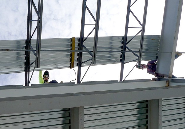 Two construction workers install part of the roof of the maintenance bay at Island Transit’s new headquarters.