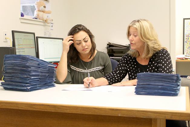 Malissa Taylor and Joanne Pelant of the Island County Housing Support Center examine client files. On their left and right are 121 files of clients on the housing support list. The stack on the left shows how many people are awaiting referrals and exemplifies the tough situation the support center faces.