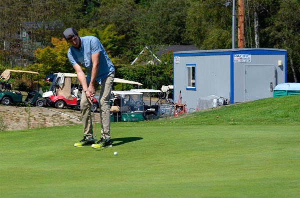 Seattle resident Matt Dawson sinks a putt at Holmes Harbor Golf Course on Monday. Behind him is the make-do pro shop that resulted from a dispute with the owner of the clubhouse. The course and the clubhouse are for sale