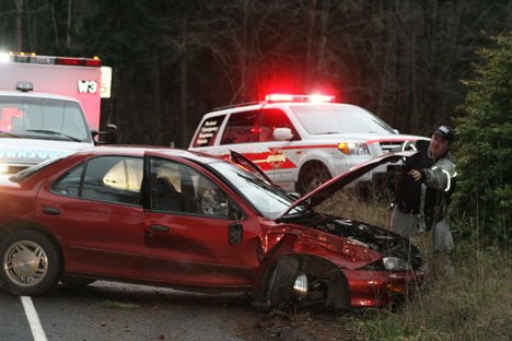 An emergency responder from Fire District 3 examines damage to a Chevy Cavalier that hit a power pole near the primary school Tuesday afternoon.