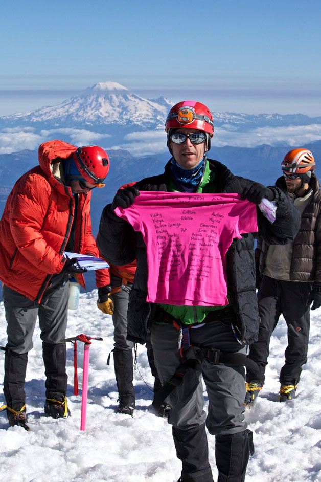 Chris Kesler of Freeland holds a thank-you T-shirt atop Mount Adams last summer. The 48-year-old man will summit Mount Baker later this month as a fundraiser for the Fred Hutchinson Cancer Research Center. Mount Rainier looms in the background.