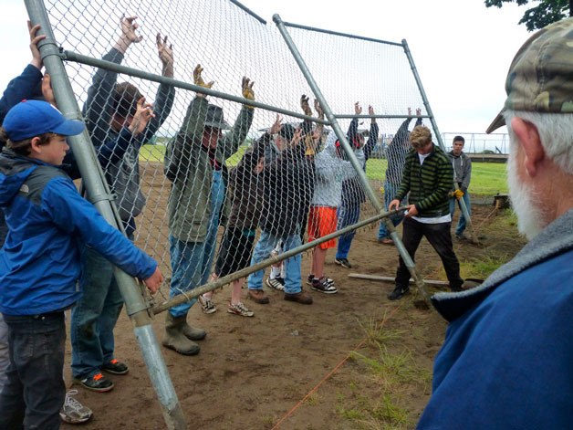 Pony League players and rotary club volunteers work together to install new fencing at the Dave Mackie Park ball field.