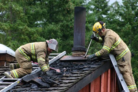 Fire District 3 Capt. Forrest Hughes and firefighter Brandon Callahan remove pieces of a burning roof at the scene of a house fire in Langley Monday morning.