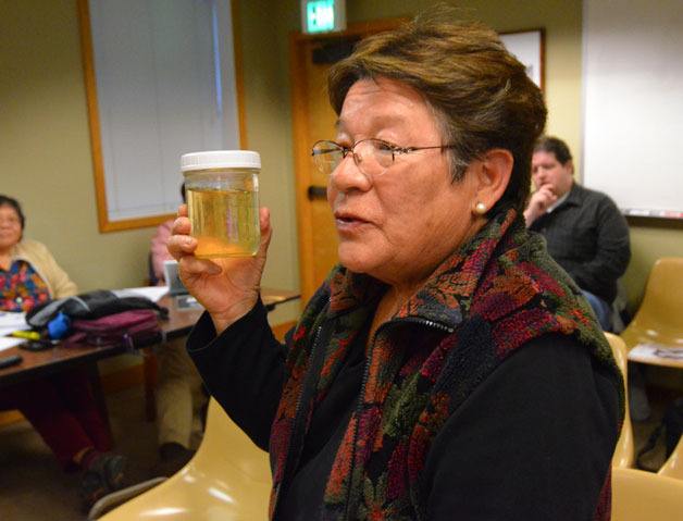Langley resident Monica Guzman presents a jar of discolored water from her home.