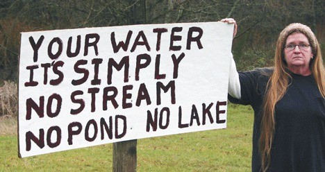 Liz Williamson stands next to a sign on her property near her disappearing pond. The sign is meant for county officials