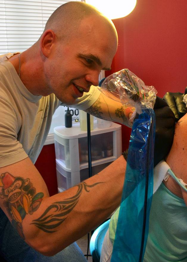 Eric Tunnell applies a tattoo on customer Kandis Jones. She traveled from Mill Creek