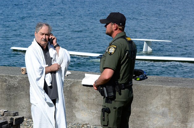Coupeville pilot Michael Clark borrows a phone from Island County Sheriff’s Office deputy Thomas Brewer. Clark’s phone was soaked when his powered glider crashed into Saratoga Passage on Friday.