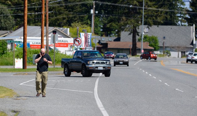 A pedestrian walks up Highway 525 in Clinton on Monday. Island County is looking at building a paved path from the ferry dock to Ken’s Korner.