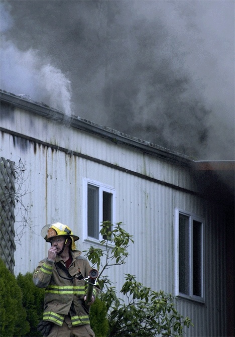 Firefighter Steve Scoles radios a fellow firefighter as he prepares a fire hose to attack a fire at a Clinton home Sunday afternoon.