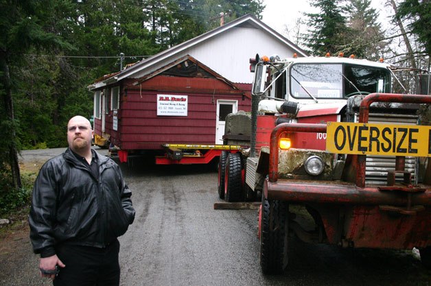 Ken Preston waits for his new house to be moved up Fiske Road to his driveway on Tuesday. He and his wife bought the house for $1 and moved it about a mile to their property.