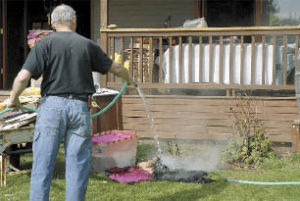 Jim Hyde sprays water on smoldering clothing after firefighters left Thursday morning.