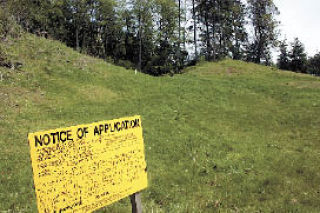 A yellow Island County application sign stands on a grassy plot of land in Freeland where a developer is proposing a warehouse and storage facility that has some residents concerned.