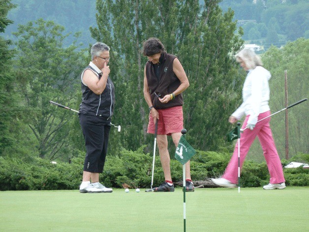 Diane Anderson and Cinday Merrit examine their putts as Teri Hagstom walks across the practice green.