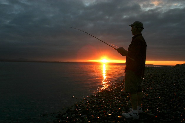 Kevin Lungren fishes from the beach at South Whidbey State Park in August as the sun sets. Though a popular sport on Whidbey