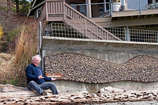 Artist Dan Freeman poses in front of his rock wave sculpture which he was asked to design and fabricate in order to cover some unsightly drain-pipe holes along a beach wall in Freeland.