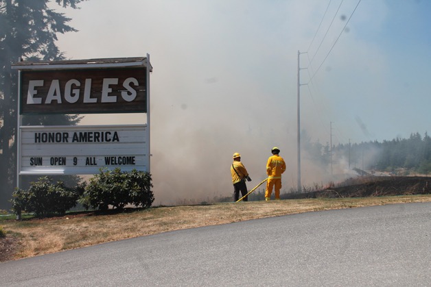 Firefighters guard the Eagles Aerie on South Whidbey Friday after a series of brushfires combined to form what officials called the largest on the South End since the 1990s. Police are investigating the cause.