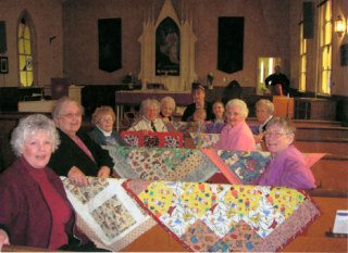 The WELCA group sits with some of Effie Higgins’ latest baby quilts. From left are Linda Alexander