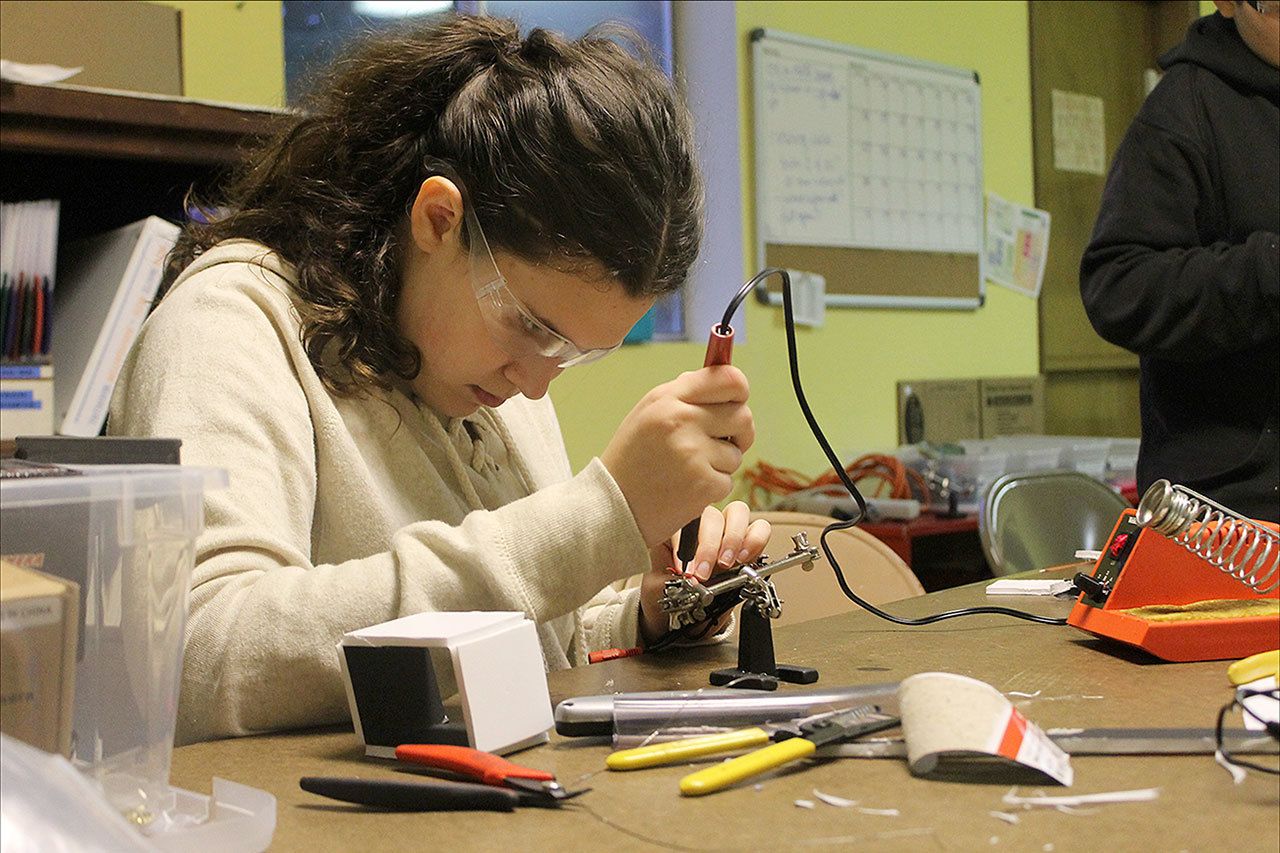Evan Thompson / The Record                                Eighth-grader Sophia Paczynski uses a soldering iron to attach wires to a dismantled auto back-up camera’s circuit board. The white box on left is for making a mold to create the camera’s waterproof casing.