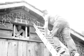 Volunteers LJ Godsey (right) and Cameron Hunt (left) climb a ladder into the attic in the process of installing a wood stove.
