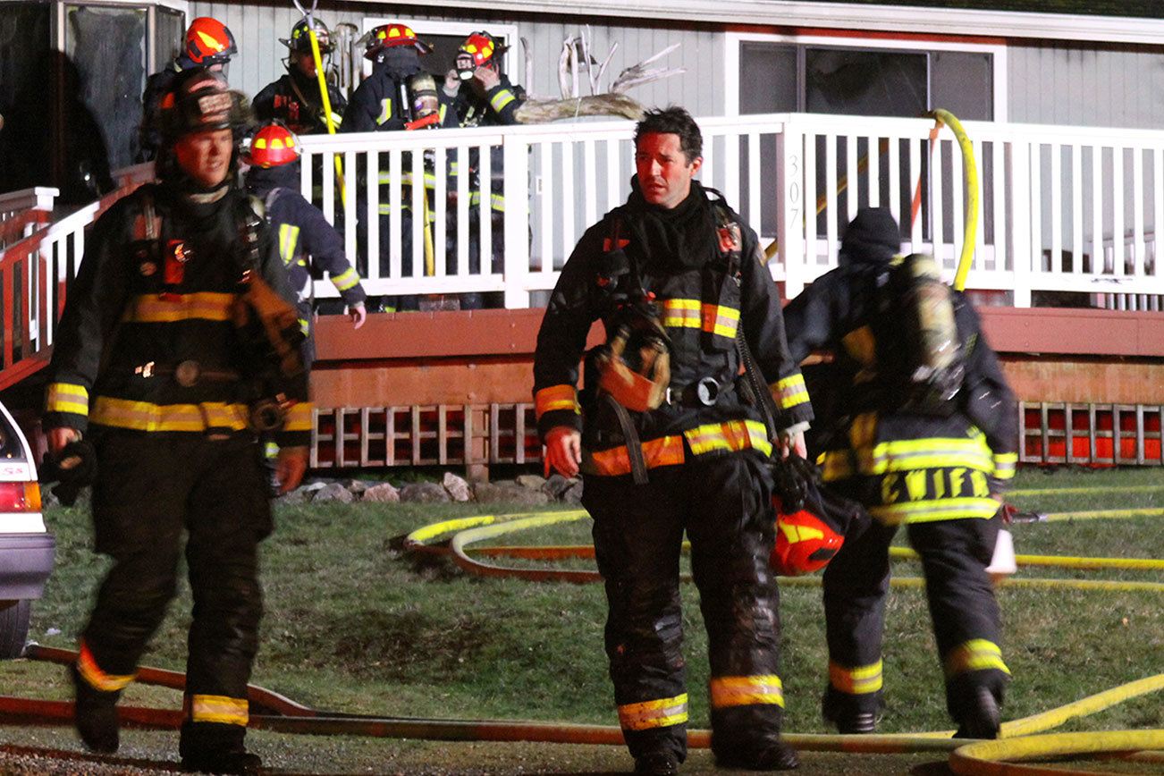 Capt. Jerry Helm, center, with Central Whidbey Fire & Rescue, walks away from a house where a man was found dead after a house fire in Coupeville Friday night. Photo by Ron Newberry/Whidbey News-Times