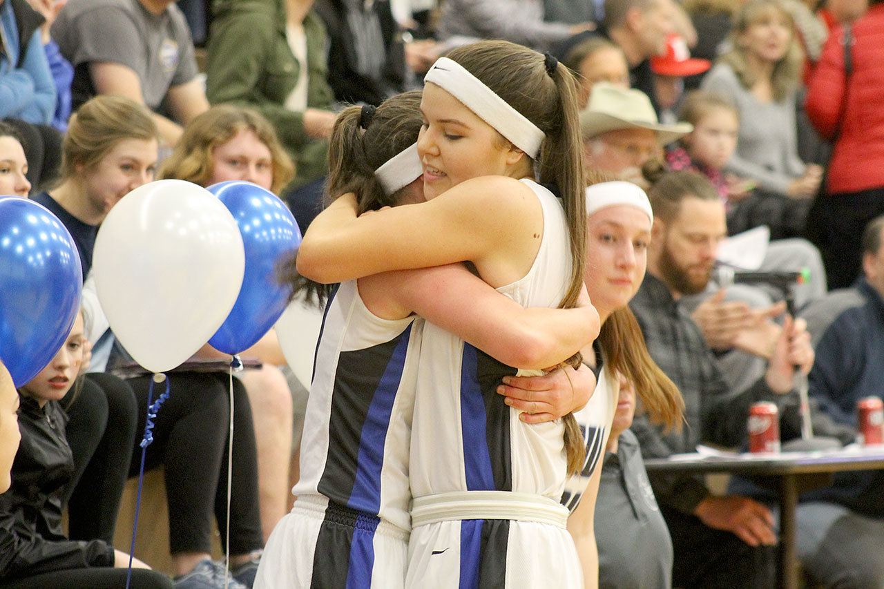Evan Thompson / The Record — South Whidbey seniors Bailey Forsyth (left) and Megan Drake (right) hug after exiting Friday night’s game against King’s on senior night. The Falcons lost 60-40.
