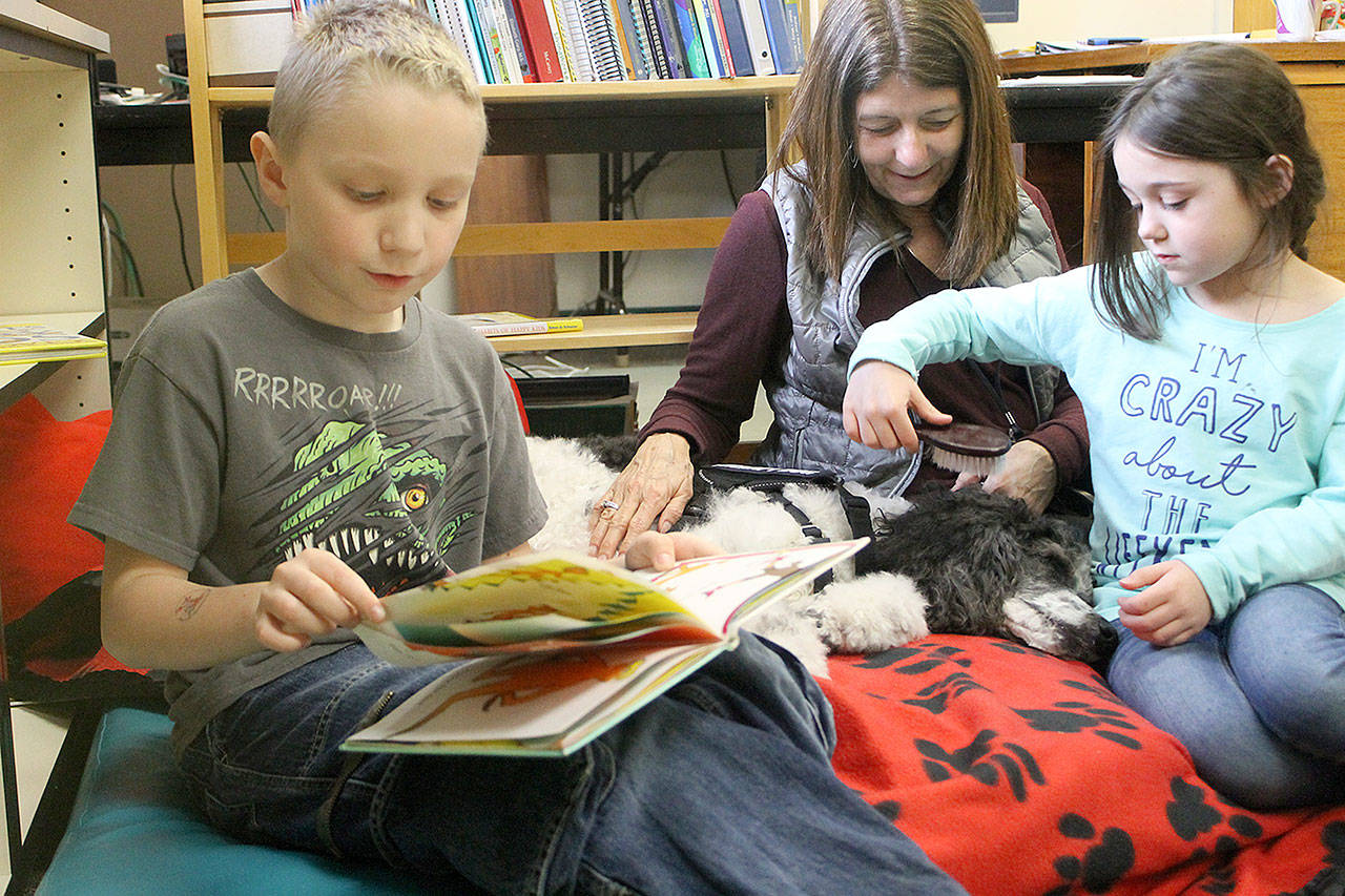 Evan Thompson / The Record — Zane Floyd, 8, reads a book to Ruby, a three-year-old parti poodle and therapy dog Reading with Rover. Nicholle Sargeant, 7, and handler LouAnn Hepp gently brushes Ruby’s fur.