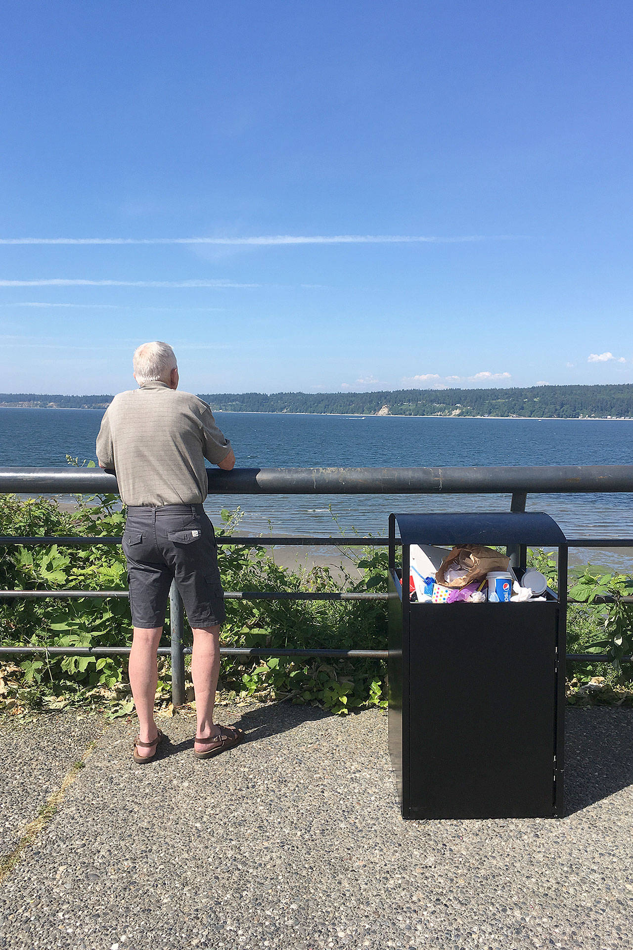 Contributed photo &mdash; An unidentified man looks across Saratoga Passage while standing next to an overflowing trash bin near Boy and Dog Park on Monday. Excess trash was the source of a headache for one business owner, while the public works department said it dropped the ball on ensuring the trash was clean.