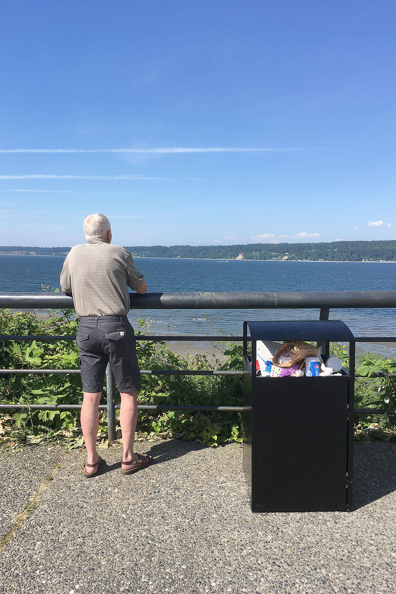 Contributed photo — An unidentified man looks across Saratoga Passage while standing next to an overflowing trash bin near Boy and Dog Park on Monday. Excess trash was the source of a headache for one business owner, while the public works department said it dropped the ball on ensuring the trash was clean.