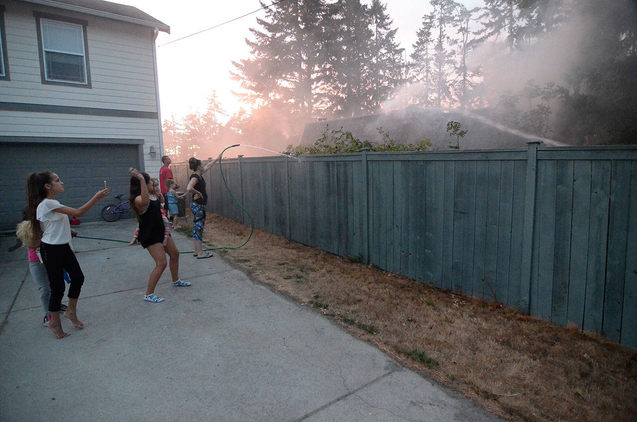 Justin Burnett/The Record — Amiee Brookhart hoses down her fence while firefighters work to extinguish a house fire next door.