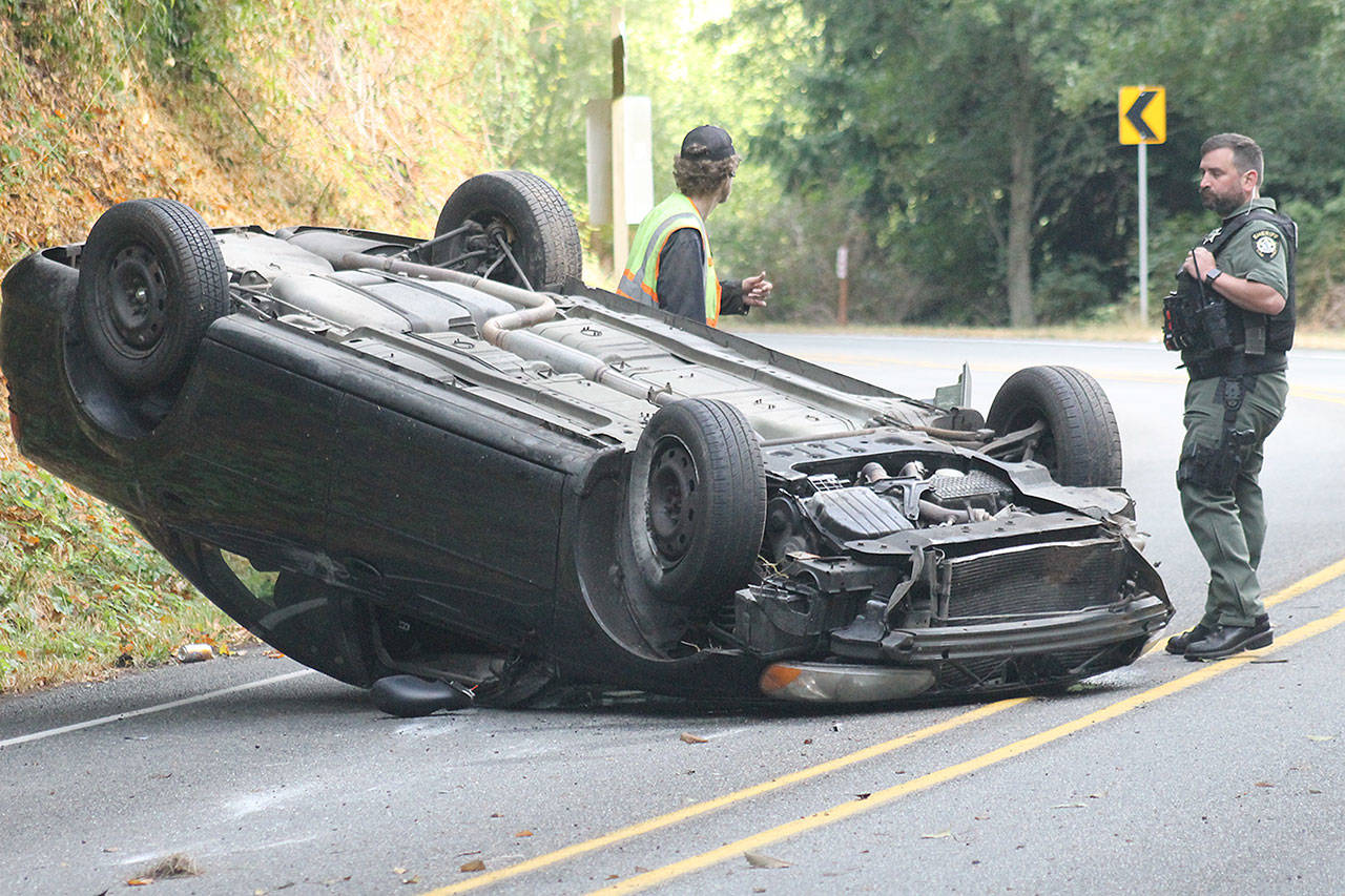 Evan Thompson / The Record &mdash; An employee with Shorty&rsquo;s Towing and Deputy Brent Durley of the Island County Sheriff&rsquo;s Office examine Julian Mozee-Rose&rsquo;s Dodge Stratus, which crashed on Monday morning on Bob Galbreath Road.