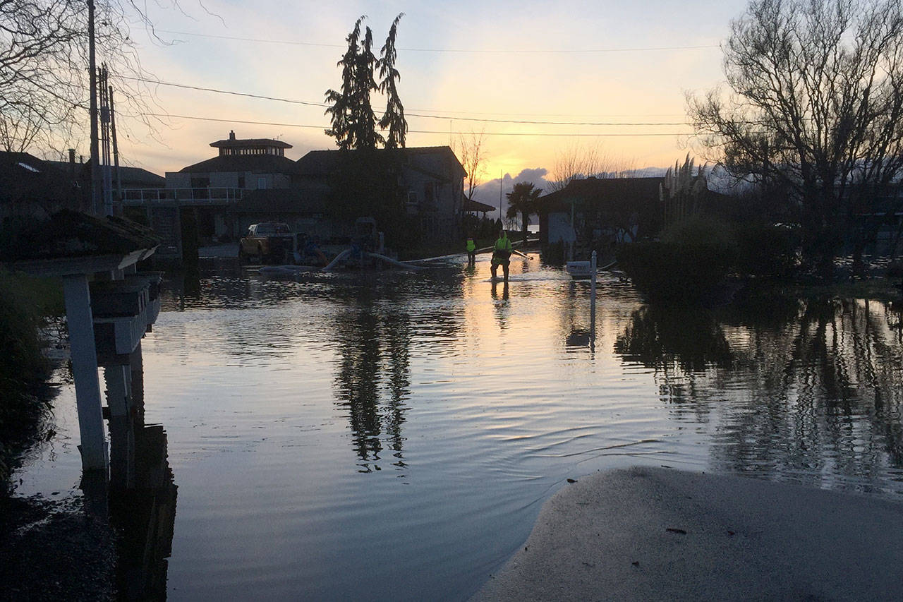 Justin Burnett/The Record &mdash; Island County Public Works employees slog through flood waters at the intersection of a Pine and Cedar streets in Mutiny Bay in January of 2016. The county is installing permanent pumps in the area to combat the ongoing problem.